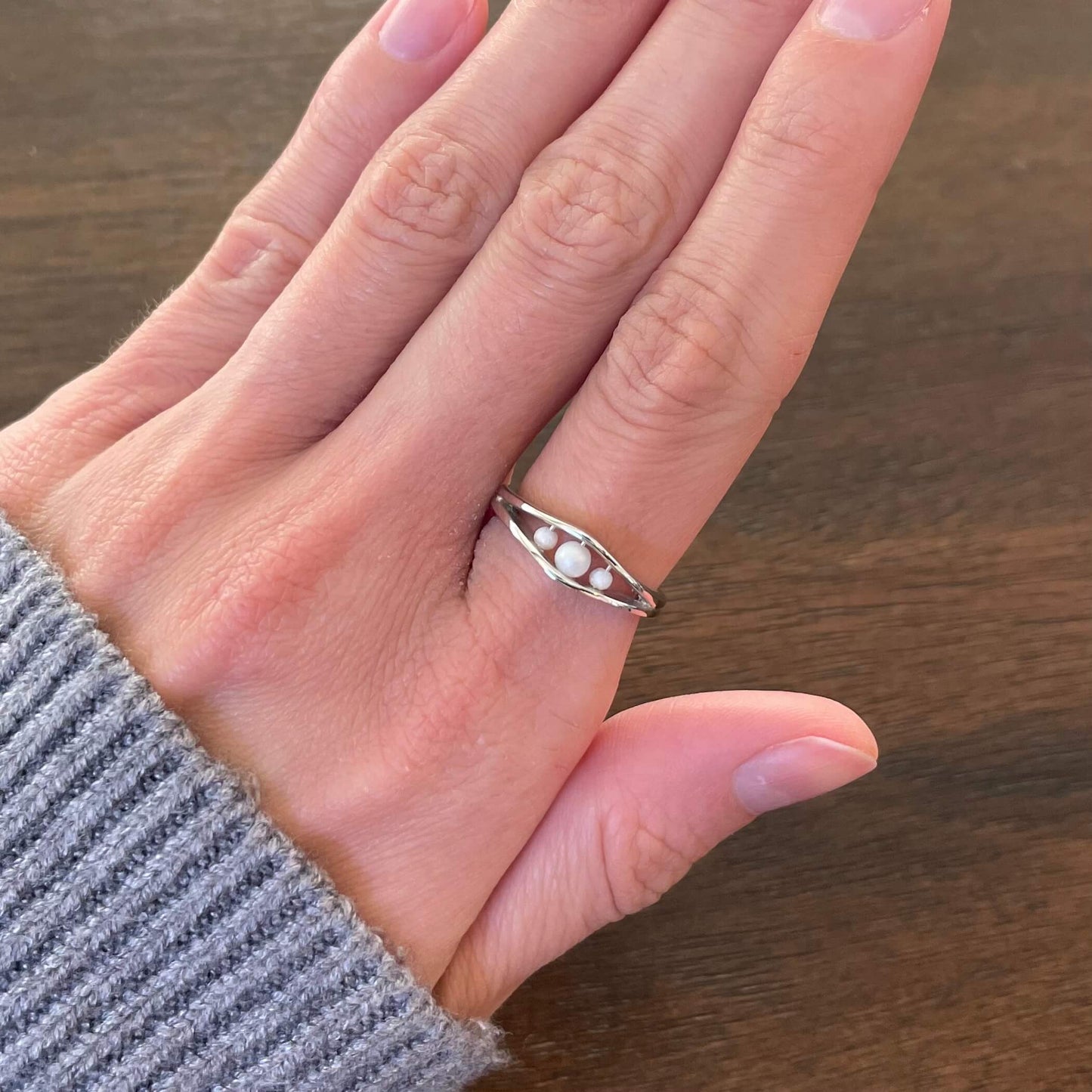 A silver Allure pearl fidget ring with three pearls worn on a finger, wearing a gray sweater