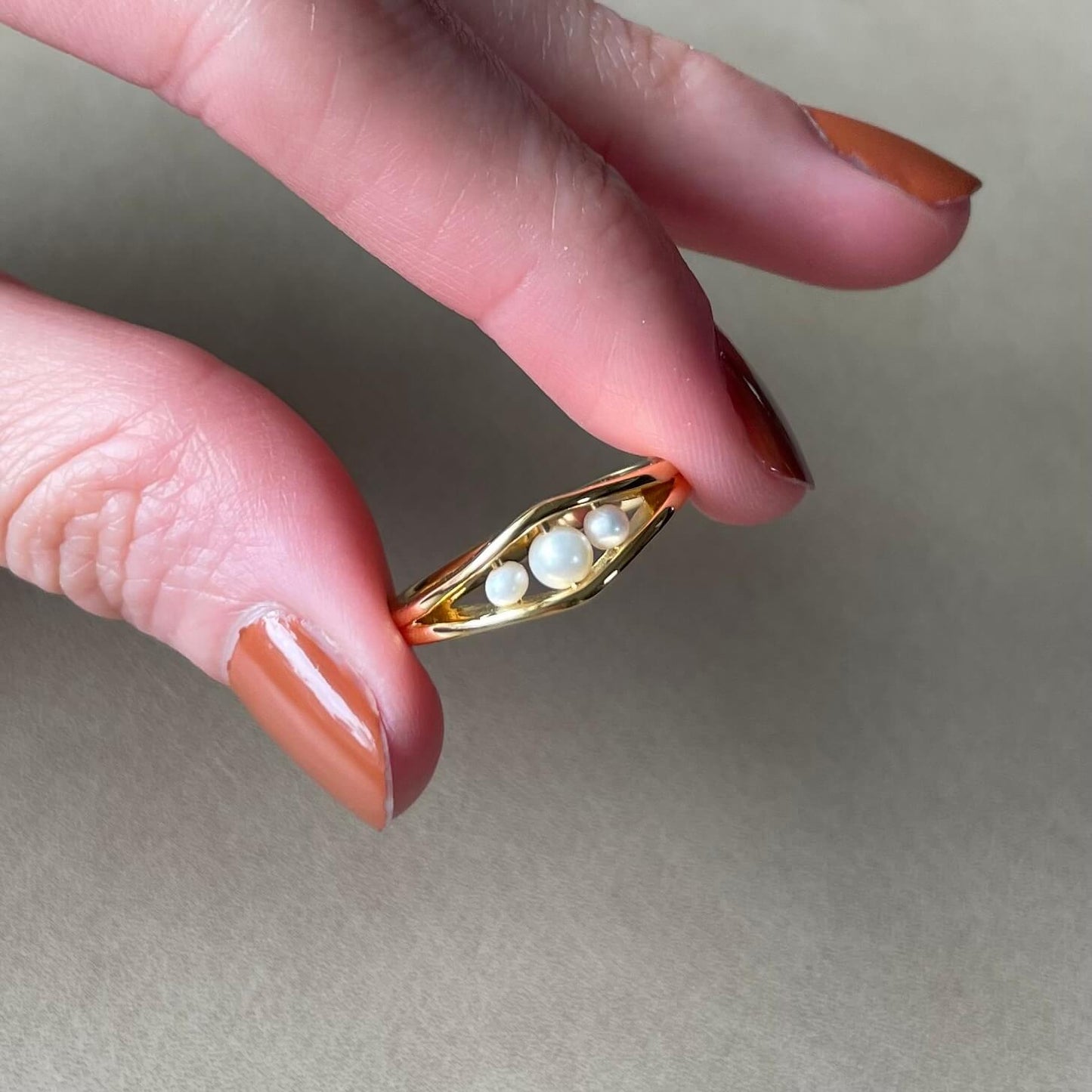 A hand holds a delicate gold Allure pearl fidget ring with three pearls between the pointer finger and thumb, ready to spin