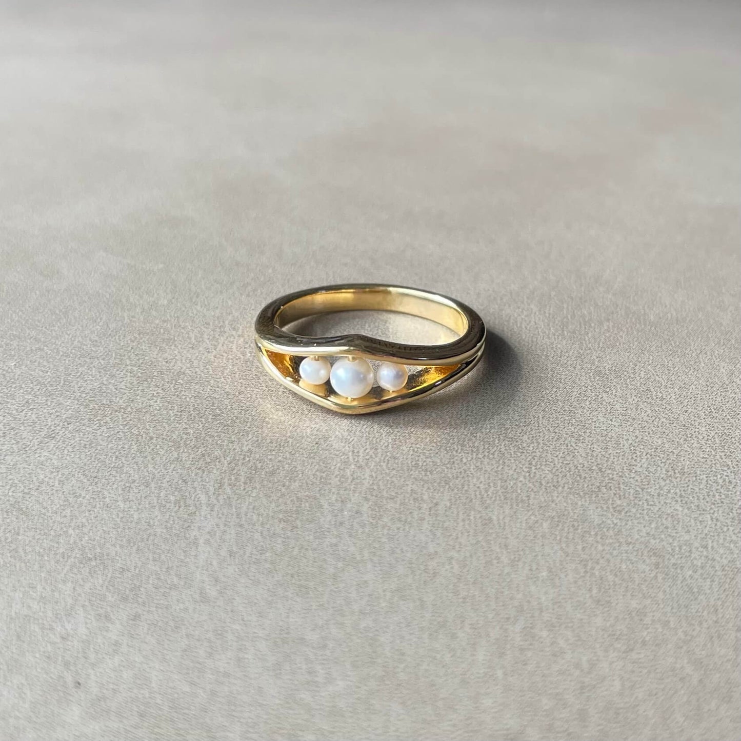 Minimalist gold Allure pearl fidget ring with three pearls resting on table with soft lighting
