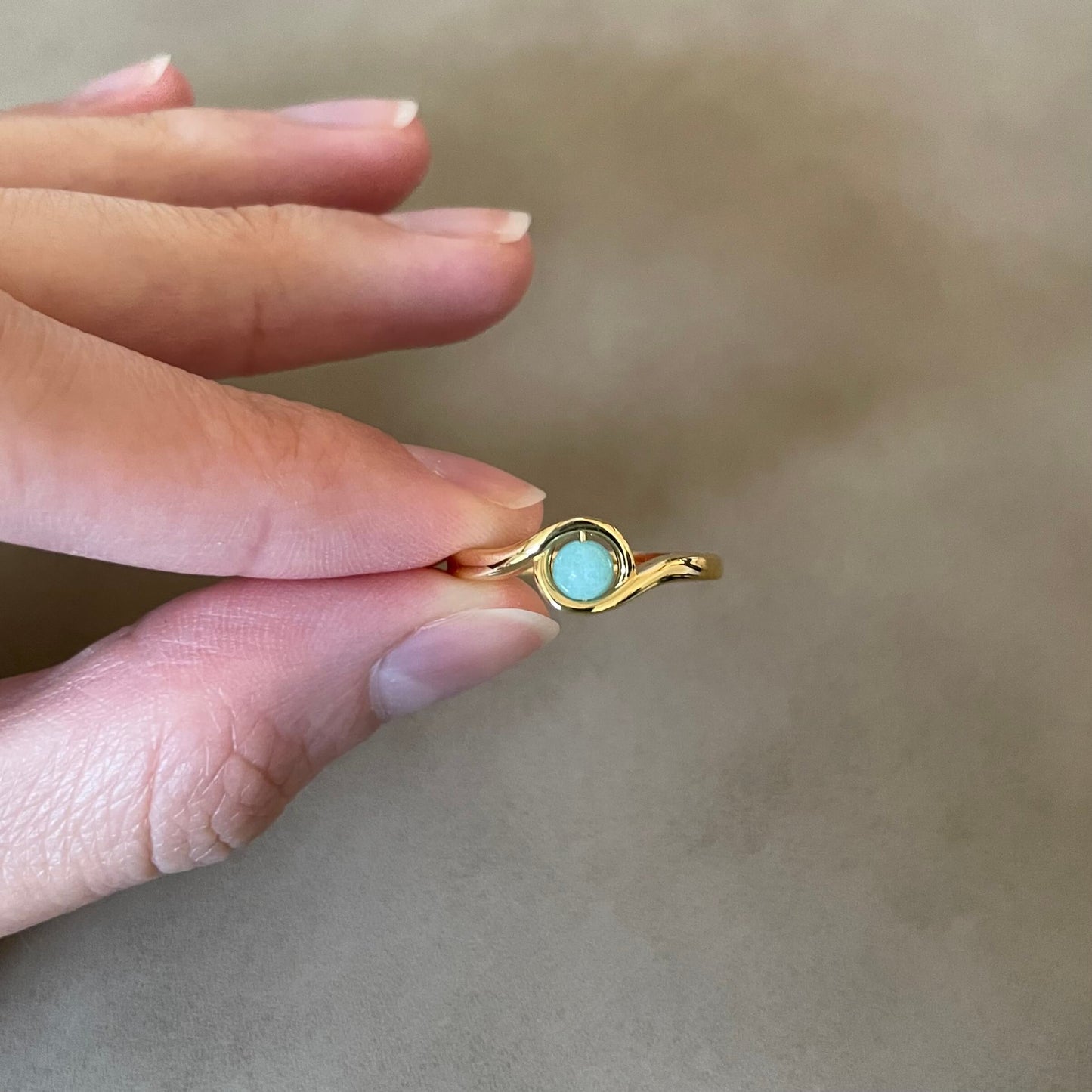 A hand holds a gold Arise amazonite fidget ring between the pointer finger and thumb, ready to spin