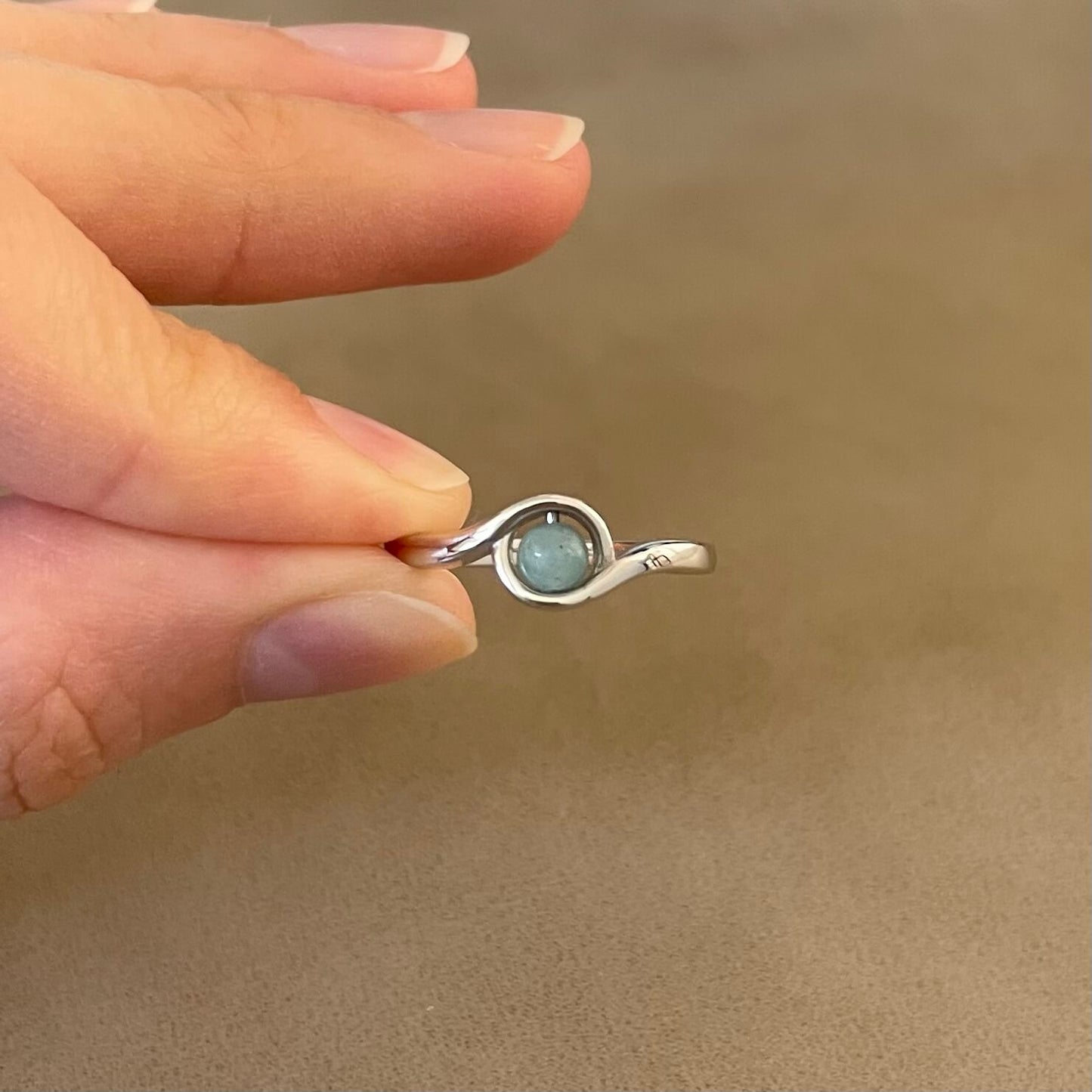A hand holds a silver Arise amazonite fidget ring, with the beautiful blue green Amazonite color visible