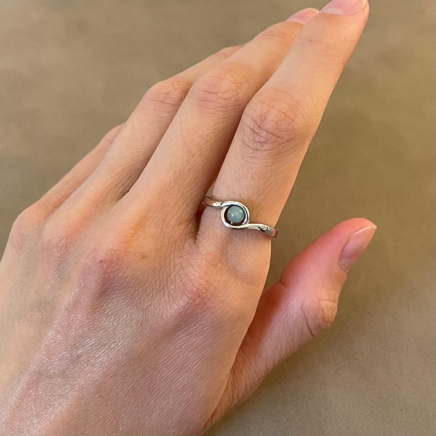 A silver Arise amazonite fidget ring worn on a finger, highlighting the light blue green gemstone's vibrant color