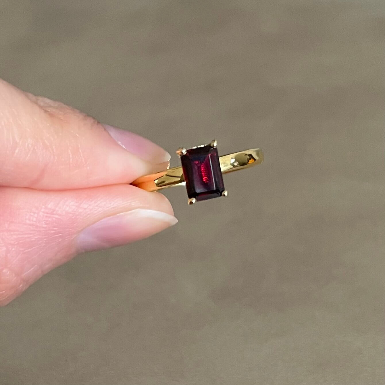 A hand holds a gold dark red Charmed garnet fidget ring between the pointer finger and thumb, ready to spin