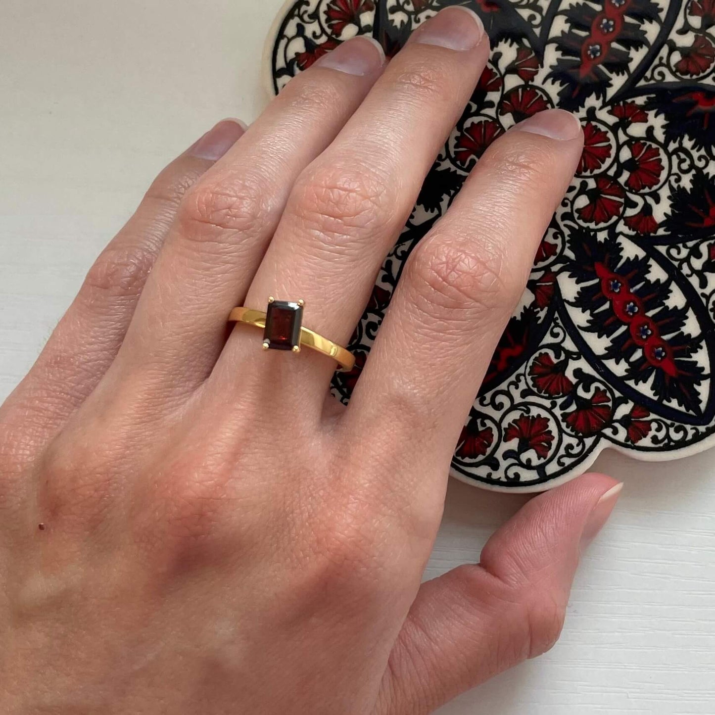 A gold deep red Charmed garnet fidget ring worn on a finger, highlighting the dark red gemstone's moody color