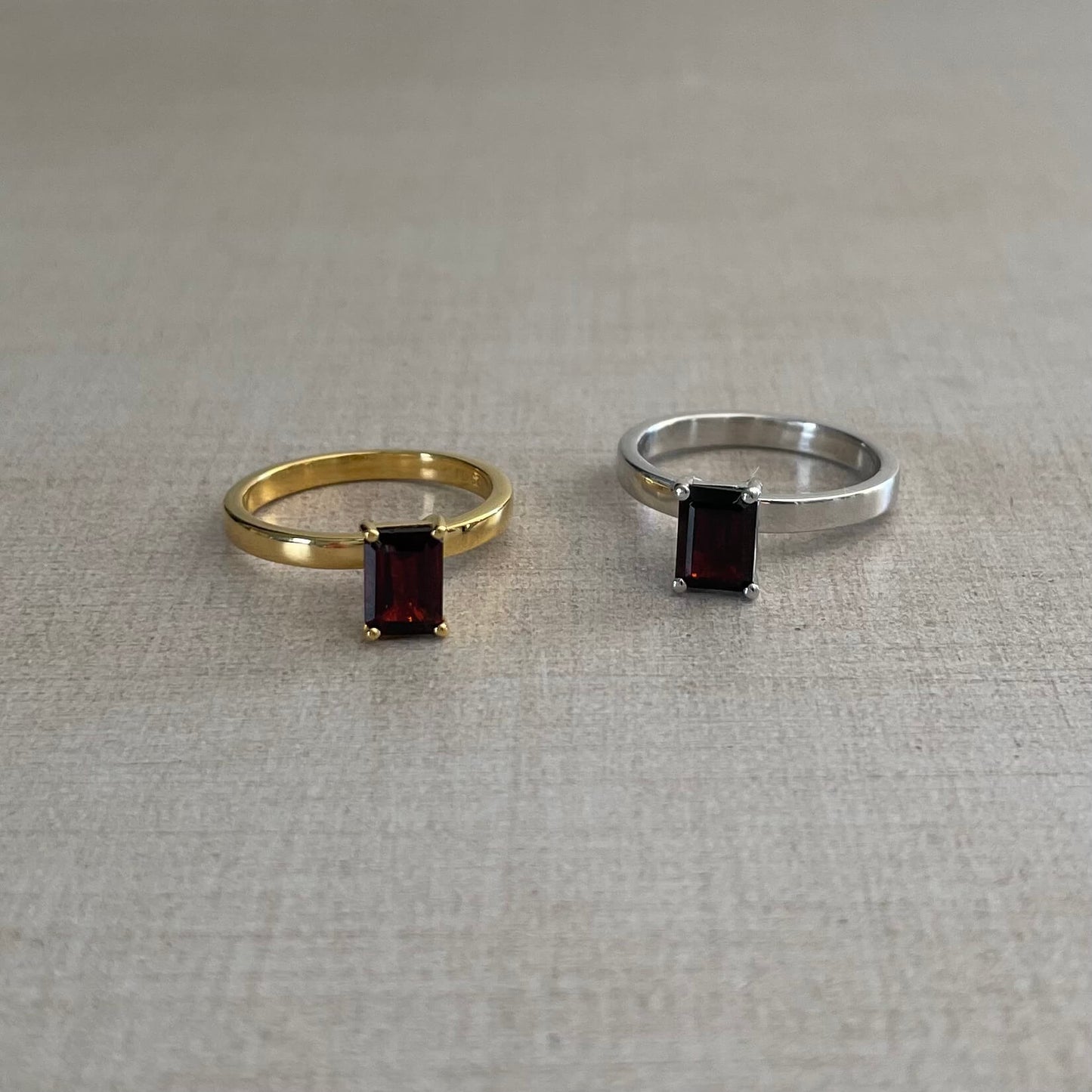 Two minimalist red Charmed garnet fidget rings in gold and silver resting on table with soft lighting