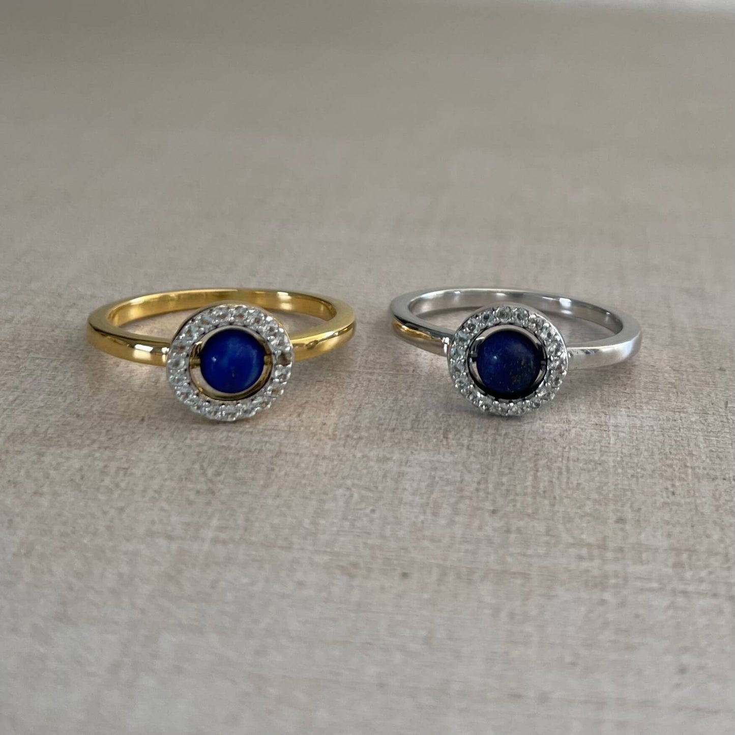 Two minimalist Enchant blue lapis fidget rings, one in gold and one in silver, resting on table with soft lighting