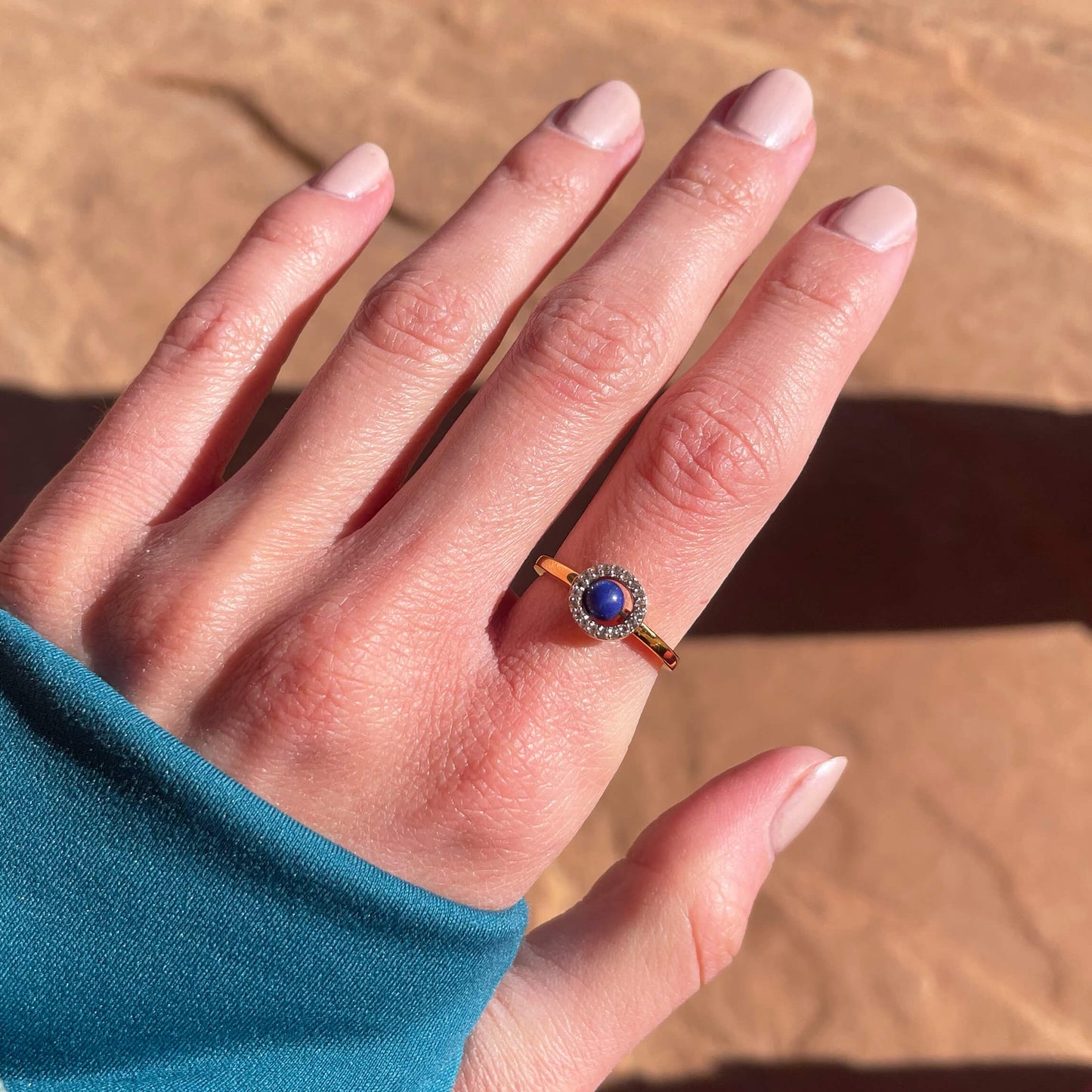 A gold Enchant blue lapis fidget ring worn on a finger, highlighting the dark blue gemstone's moody color and vibrant white topaz halo gems