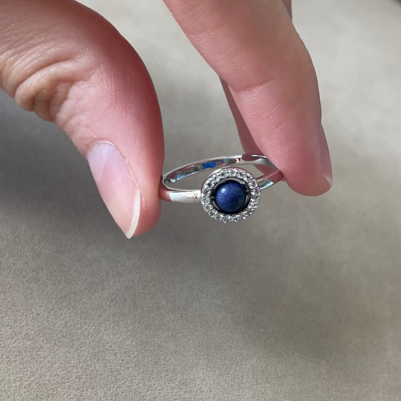 A hand holds a silver Enchant blue lapis fidget ring with vibrant white topaz gems between the pointer finger and thumb, ready to spin