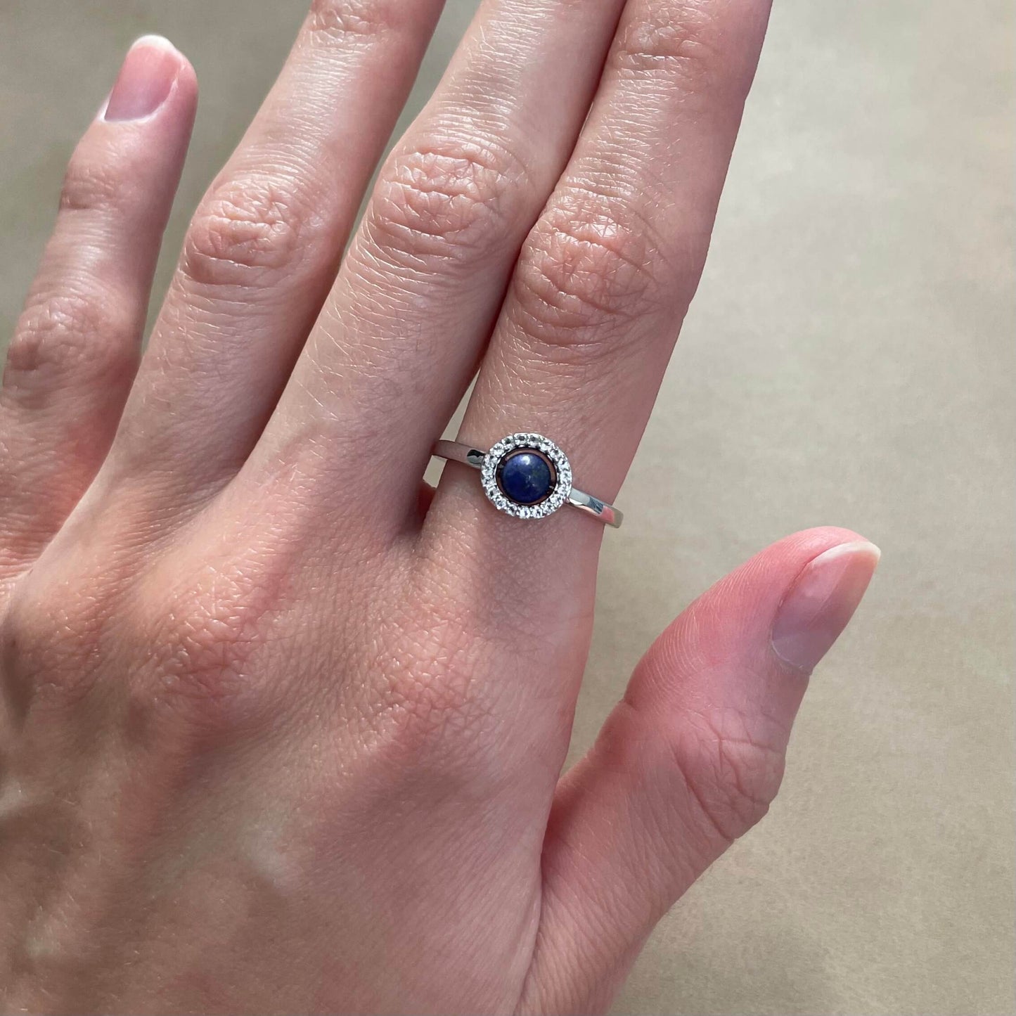 A silver Enchant blue lapis fidget ring worn on a finger, highlighting the deep blue gem and delicate white topaz halo
