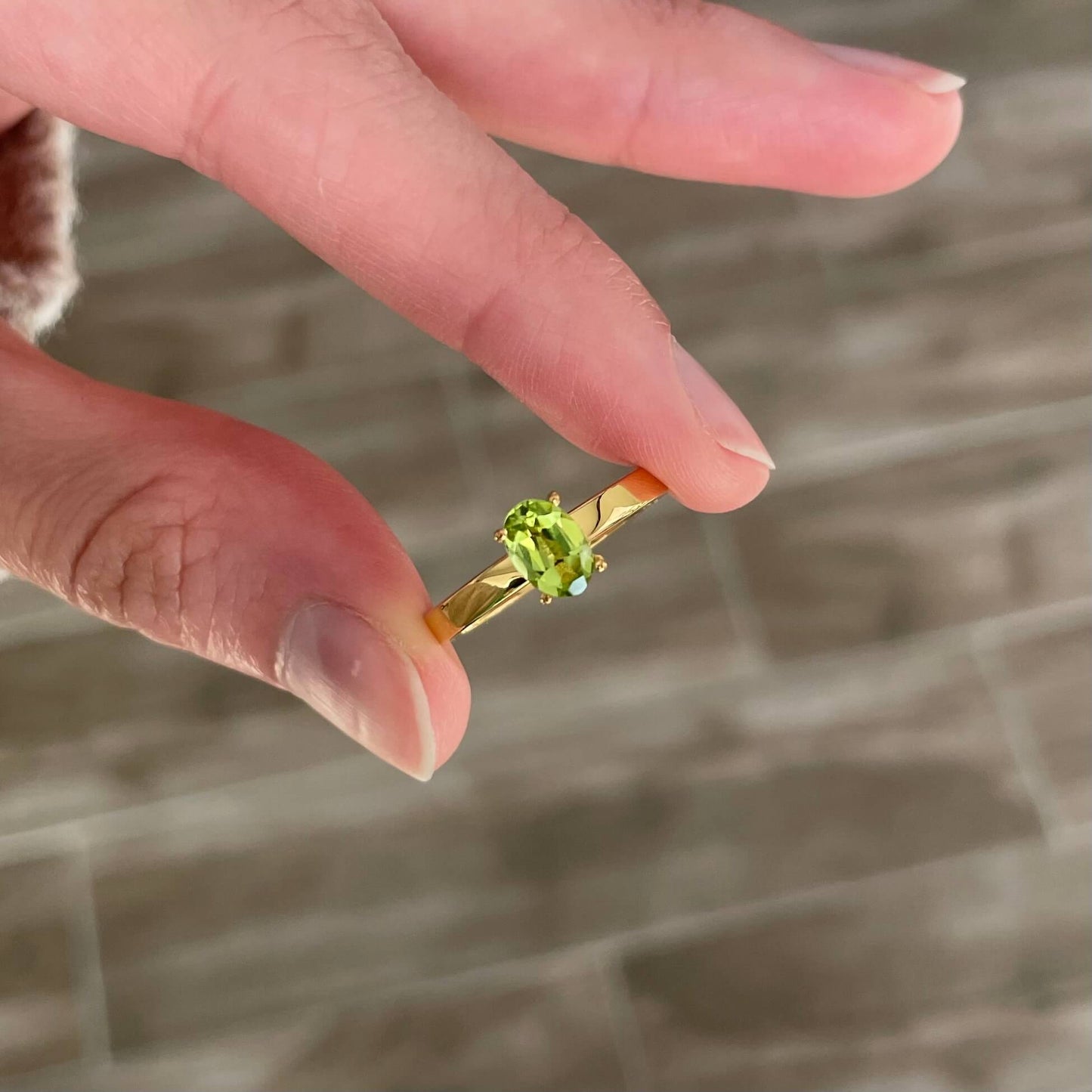 A hand holds a gold light green Enlight peridot fidget ring between the pointer finger and thumb, ready to spin