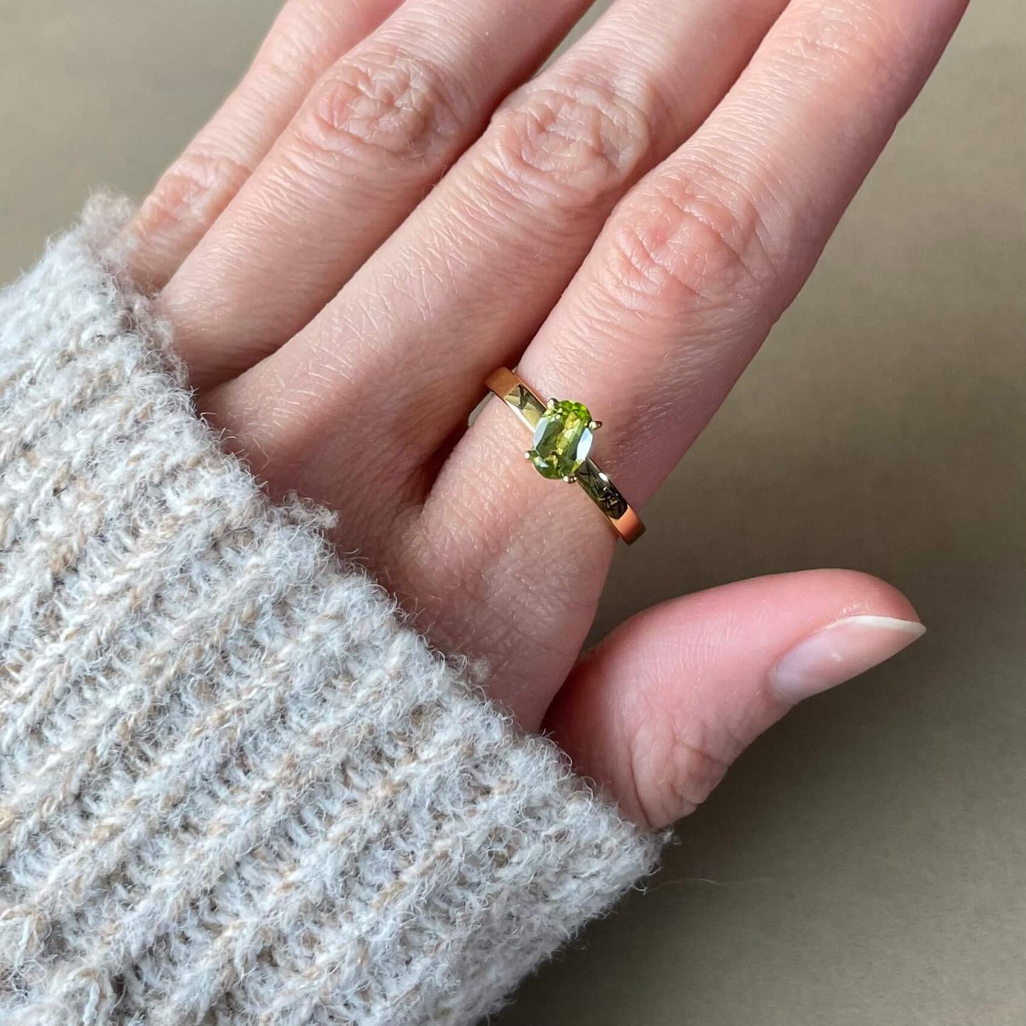 A gold Enlight peridot fidget ring worn on a finger, highlighting the green gemstone's vibrant color