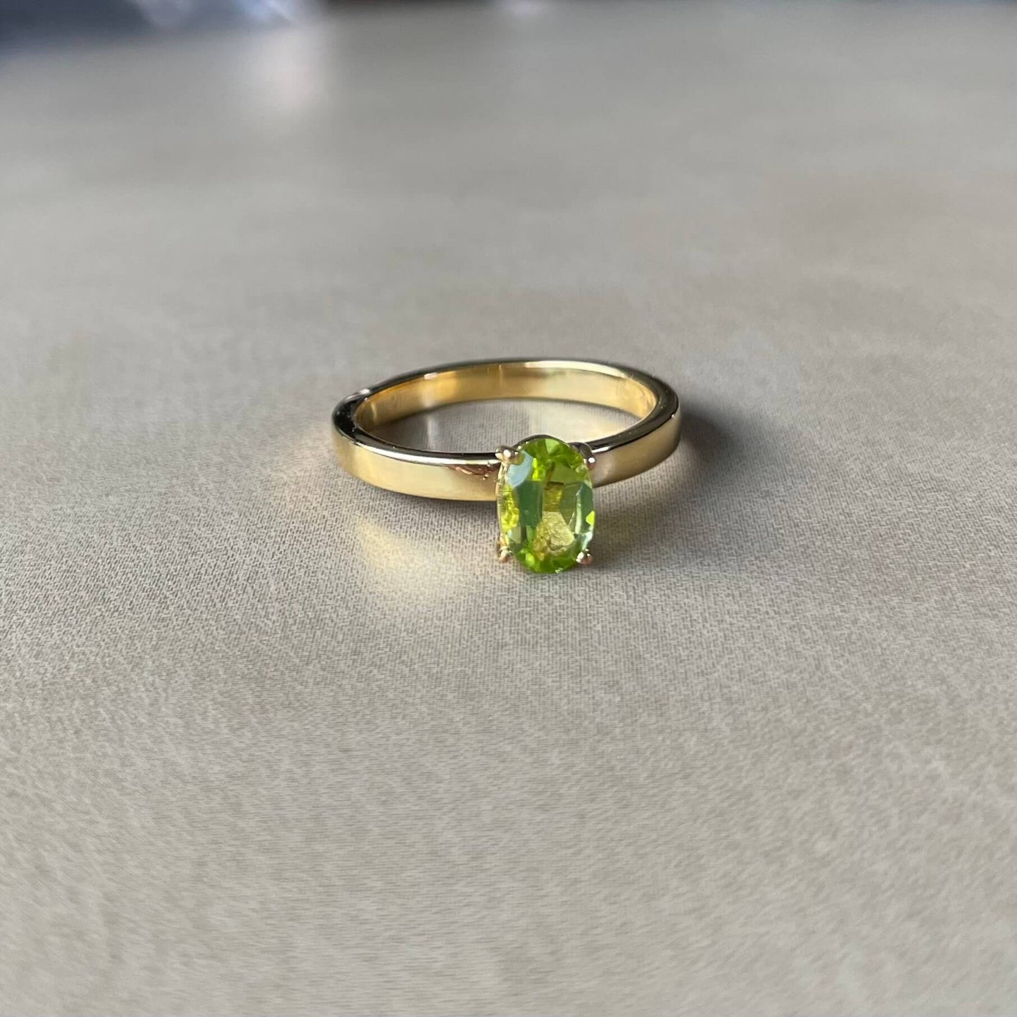 Minimalist green Enlight peridot fidget ring in gold resting on table with soft lighting