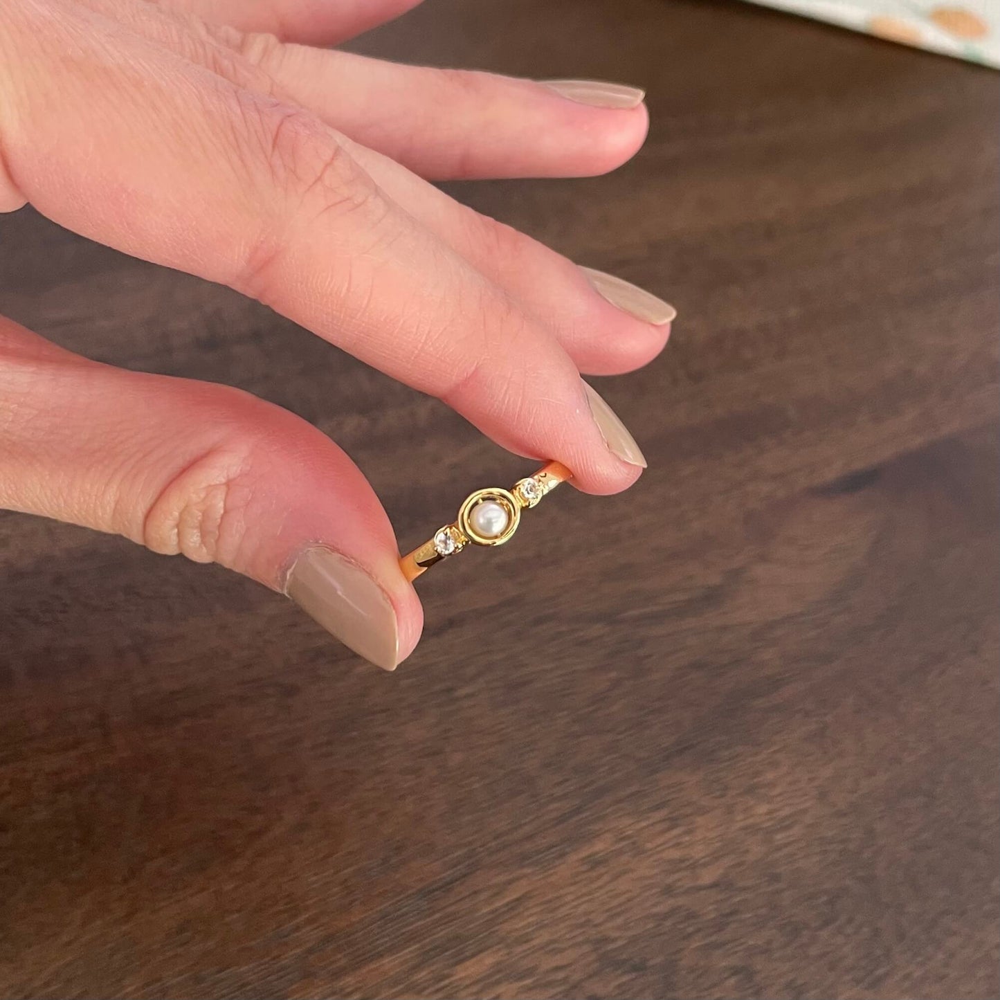 A hand holds a delicate gold Mindful pearl fidget ring with two white topaz gems between the pointer finger and thumb, ready to spin