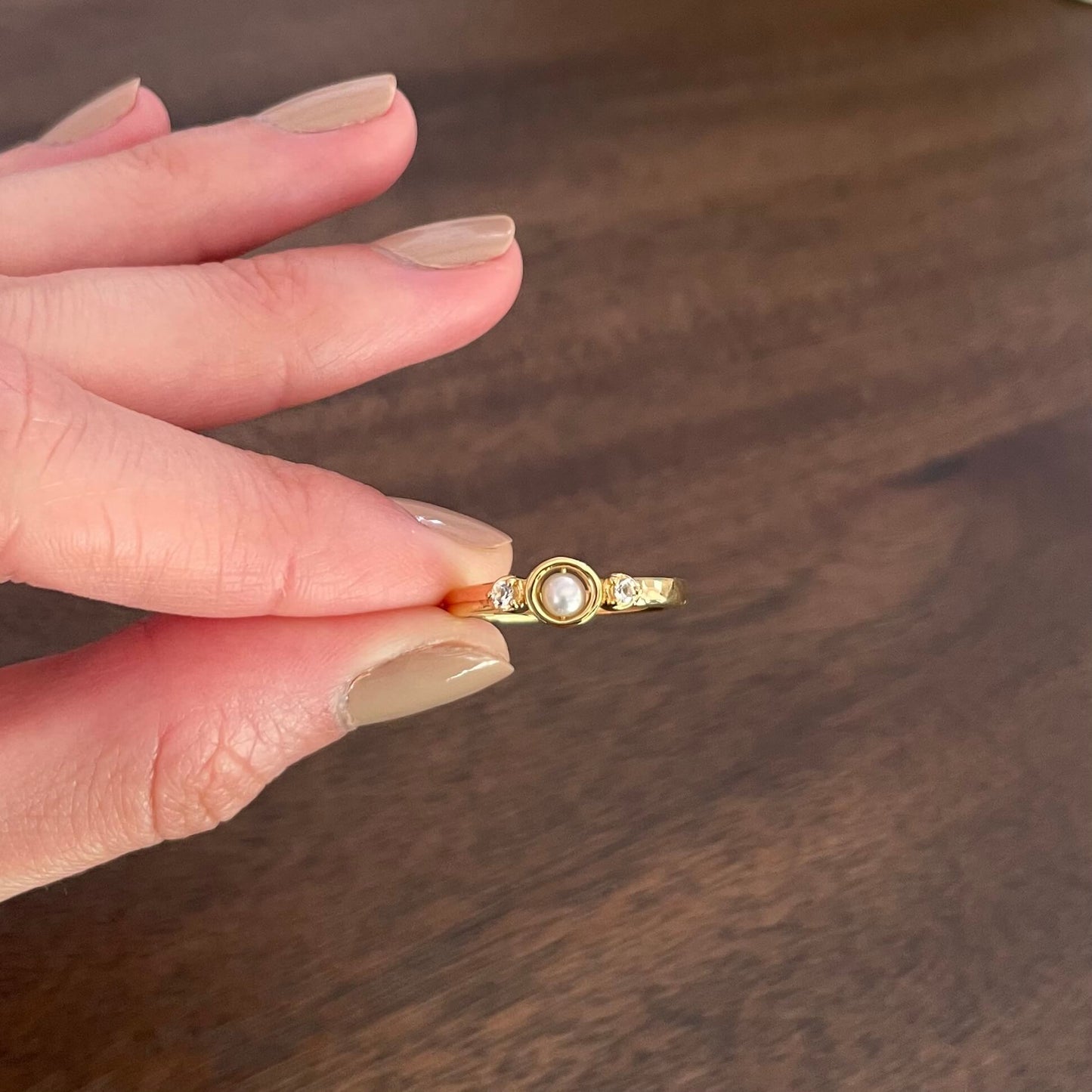 A hand holds a minimal gold Mindful pearl fidget ring with two white topaz gems between the pointer finger and thumb, ready to spin